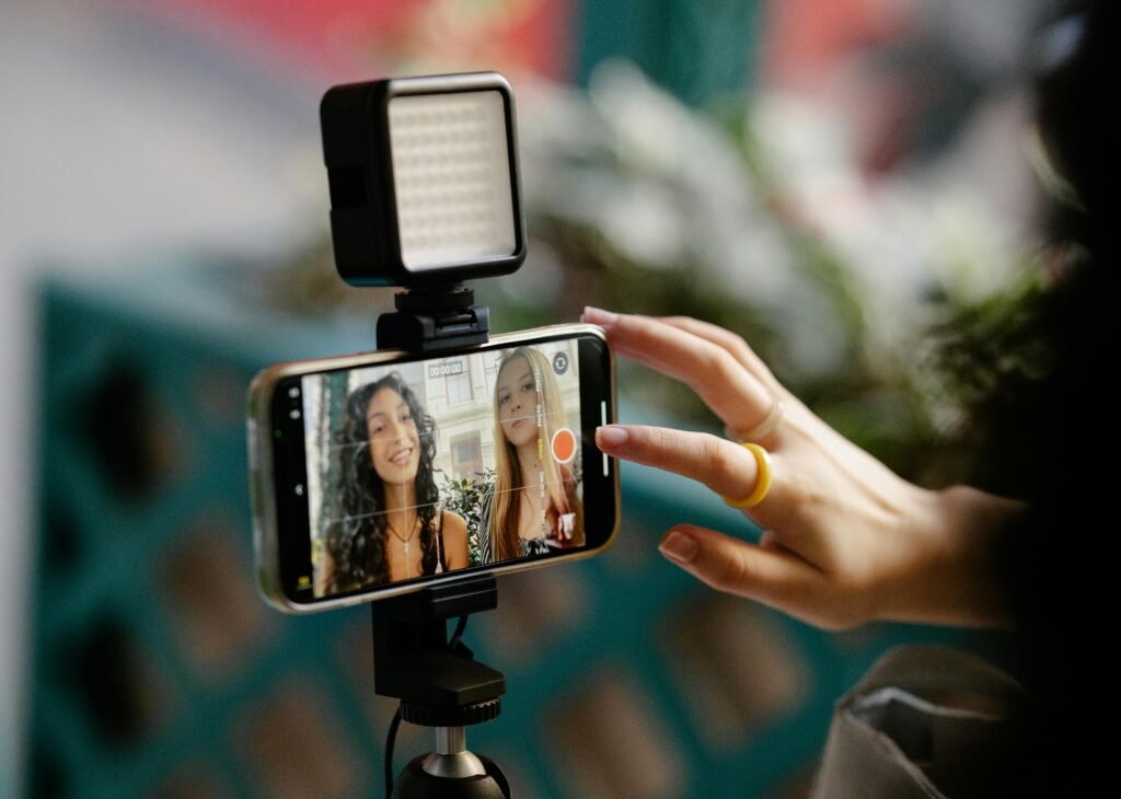 AI YouTube Channels: The Truth About Faceless Content (And Whether Viewers Actually Care) 2 Two women recording a video using a smartphone and LED light setup, illustrating modern content creation.