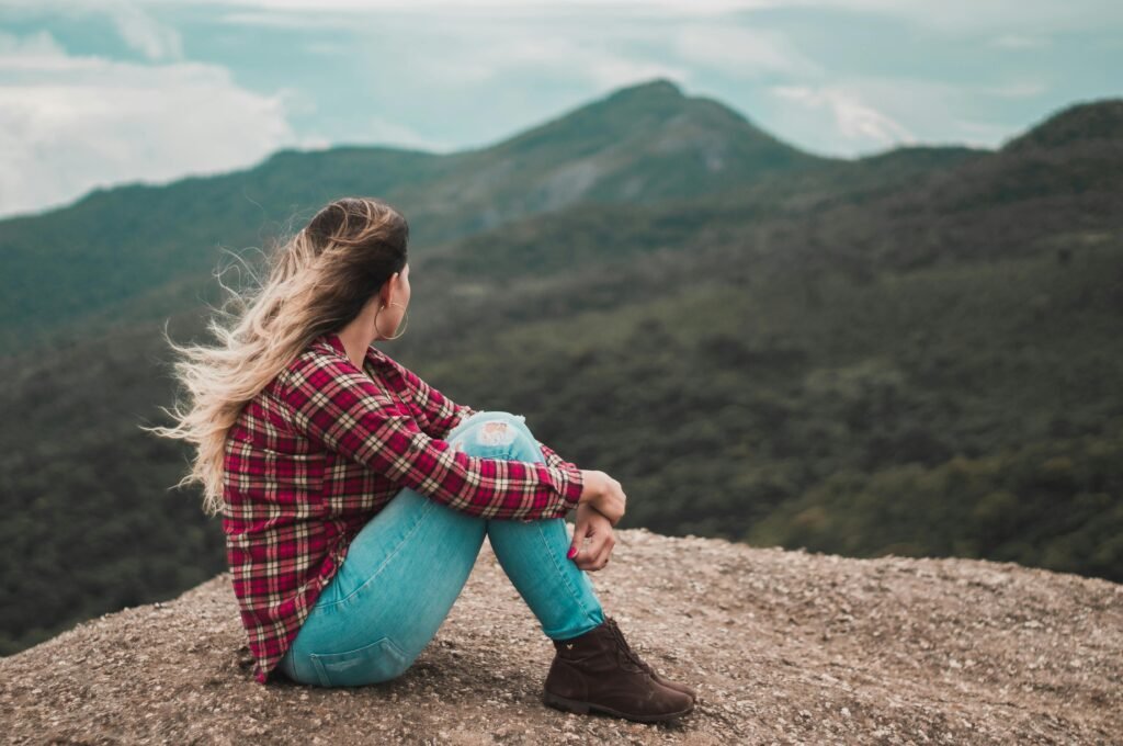 A woman in casual wear enjoys solitude on a scenic Brazilian mountain, embracing a moment of reflection.