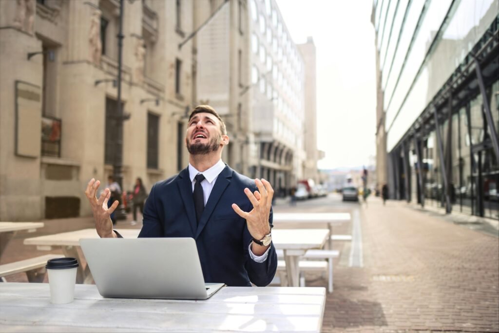 Who Won the AI Race in 2025? Ranking ChatGPT, Claude, Gemini, and Perplexity 2 Businessman in suit showing frustration at outdoor table with laptop and coffee.