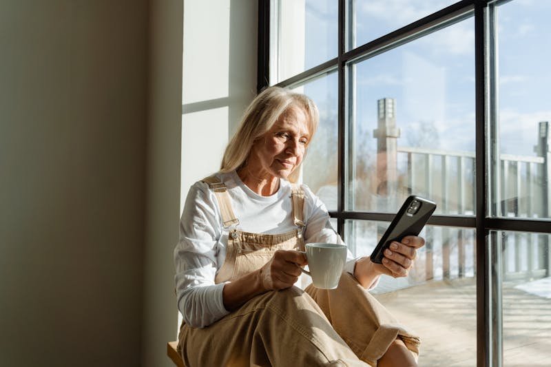 Woman relaxing with coffee and smartphone by a sunny window representing calm content consumption