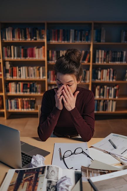 Woman feeling stressed while studying in library surrounded by books, depicting information overload