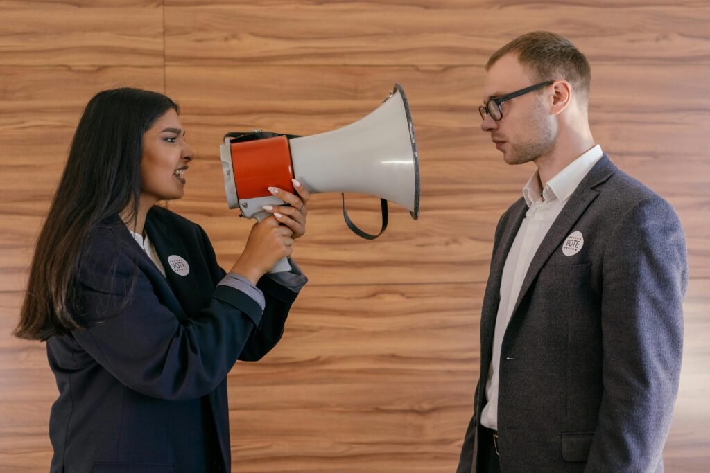 A woman using a megaphone to confront a man in a suit indoors, symbolizing political debate.