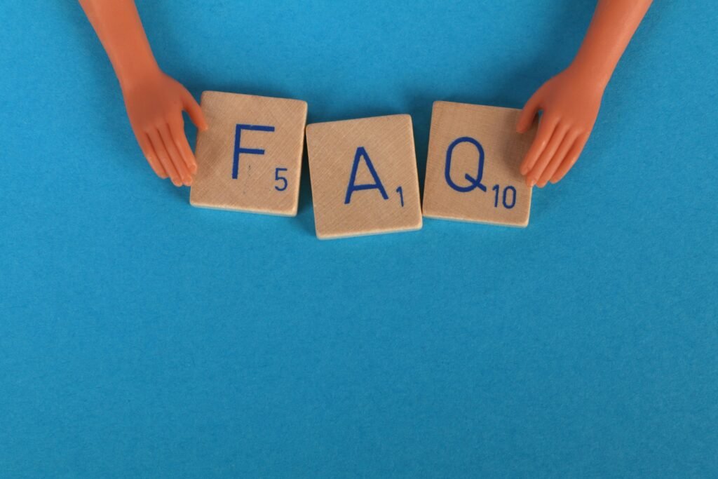 Flat lay of scrabble tiles spelling 'FAQ' with toy hands on a blue background, creating a conceptual image.