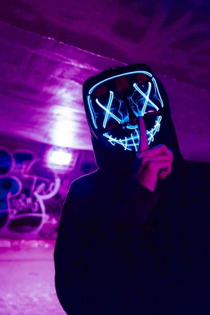 Eerie figure wearing a neon LED mask in a dimly lit urban environment, creating a mysterious atmosphere.