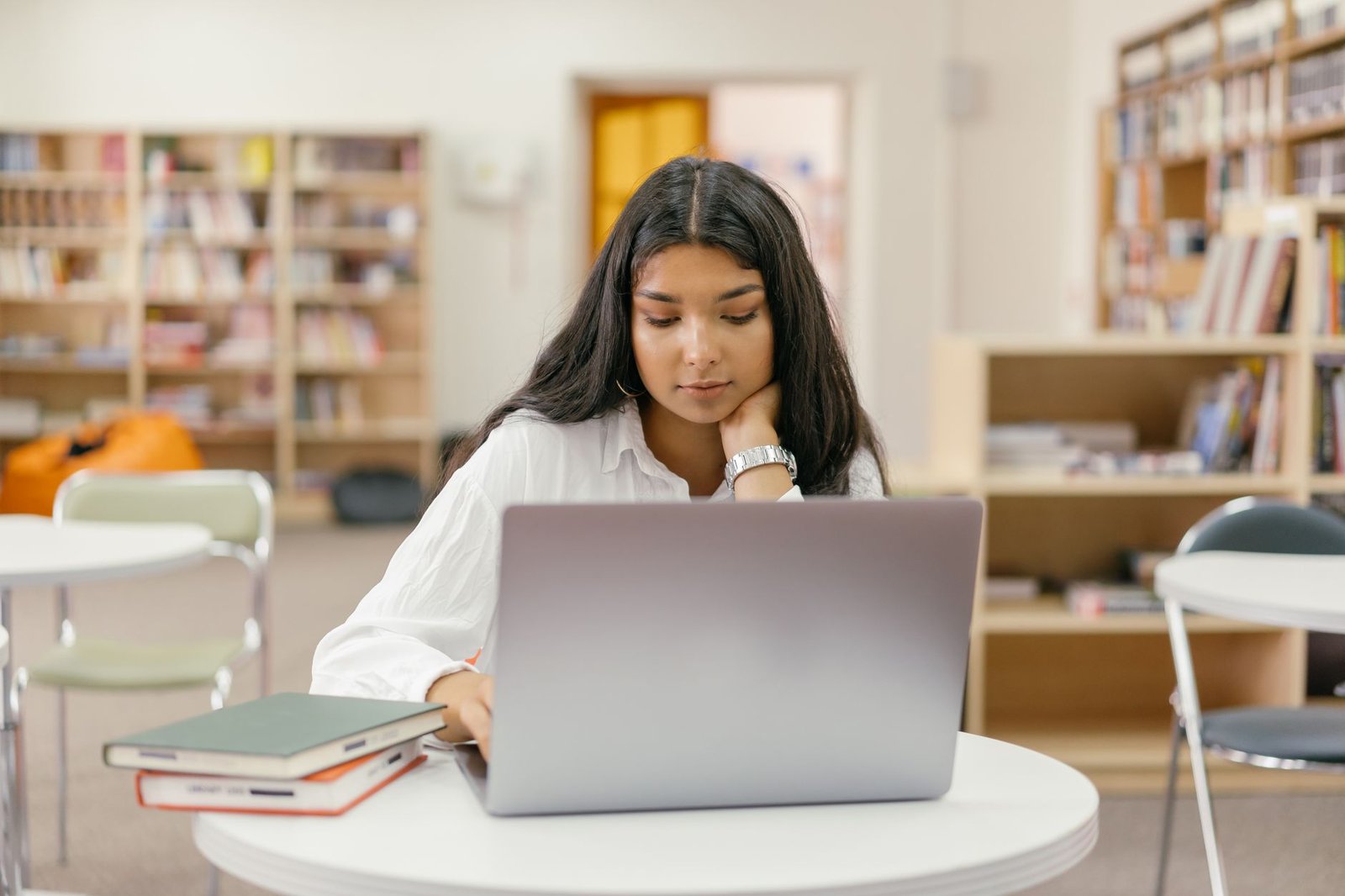 Woman studying online with a laptop and books in a library, the way Claude Academy courses fit into a normal week