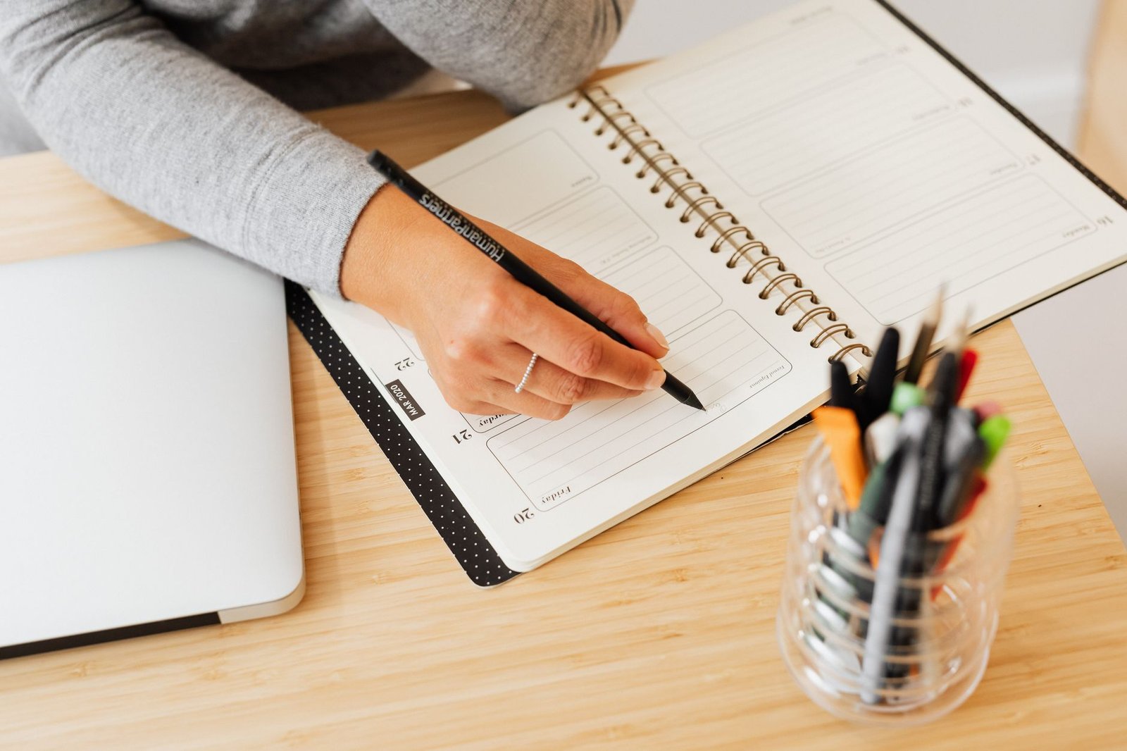 Hand writing in a planner next to a laptop, like walking through the Gemini Daily Brief setup steps