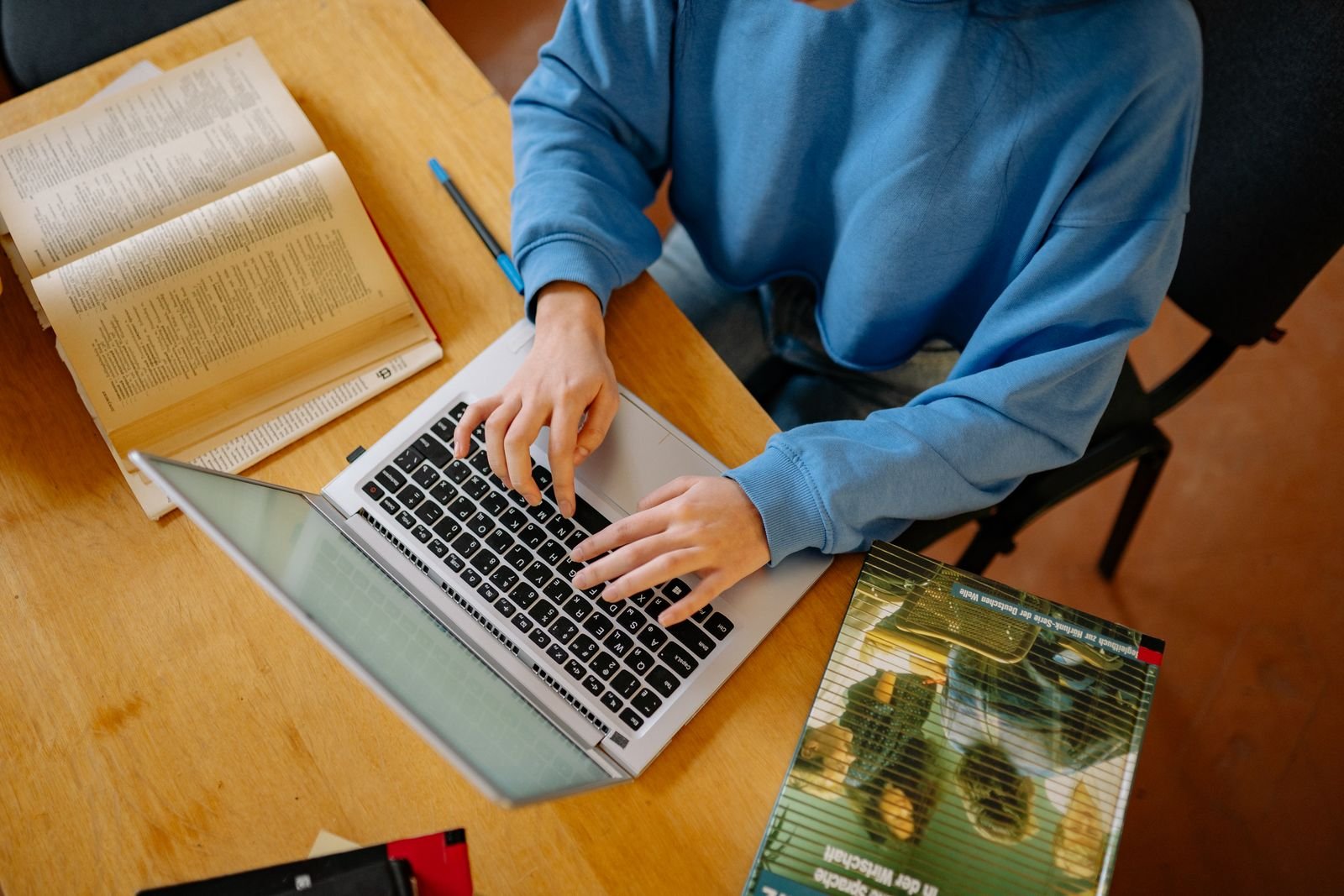Student typing on a laptop surrounded by open textbooks while studying