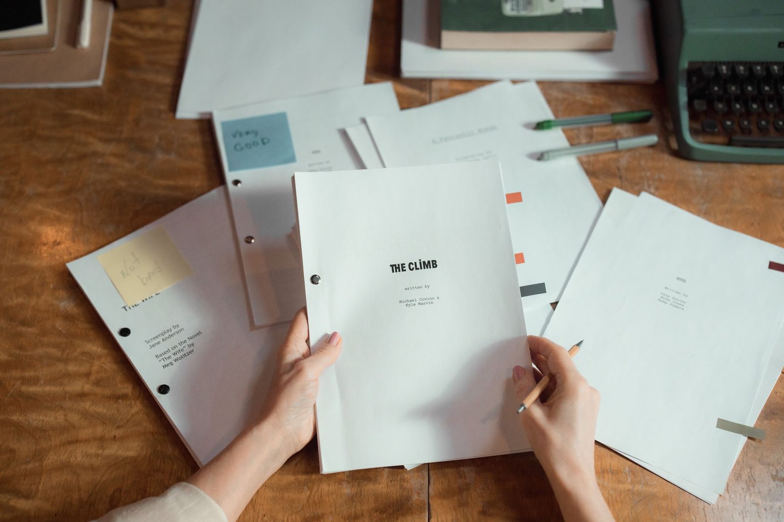Hands holding a stack of draft pages beside a typewriter