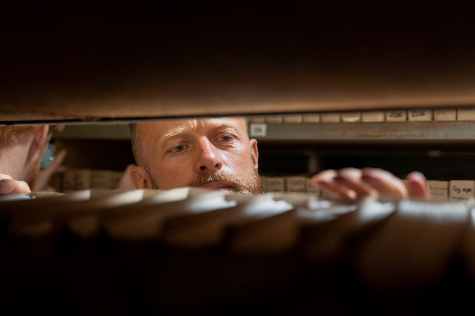 A man searches through boxes of files in an office archive room, like a reviewer working through a queue of ChatGPT chats