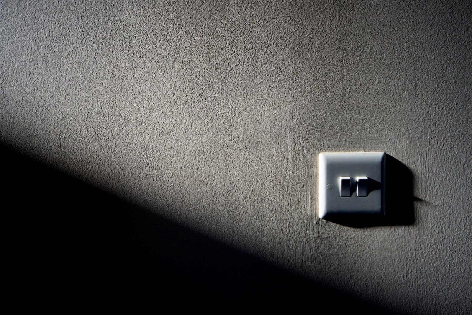 A single light switch on a textured wall, half in shadow, for the Temporary Chat option in ChatGPT