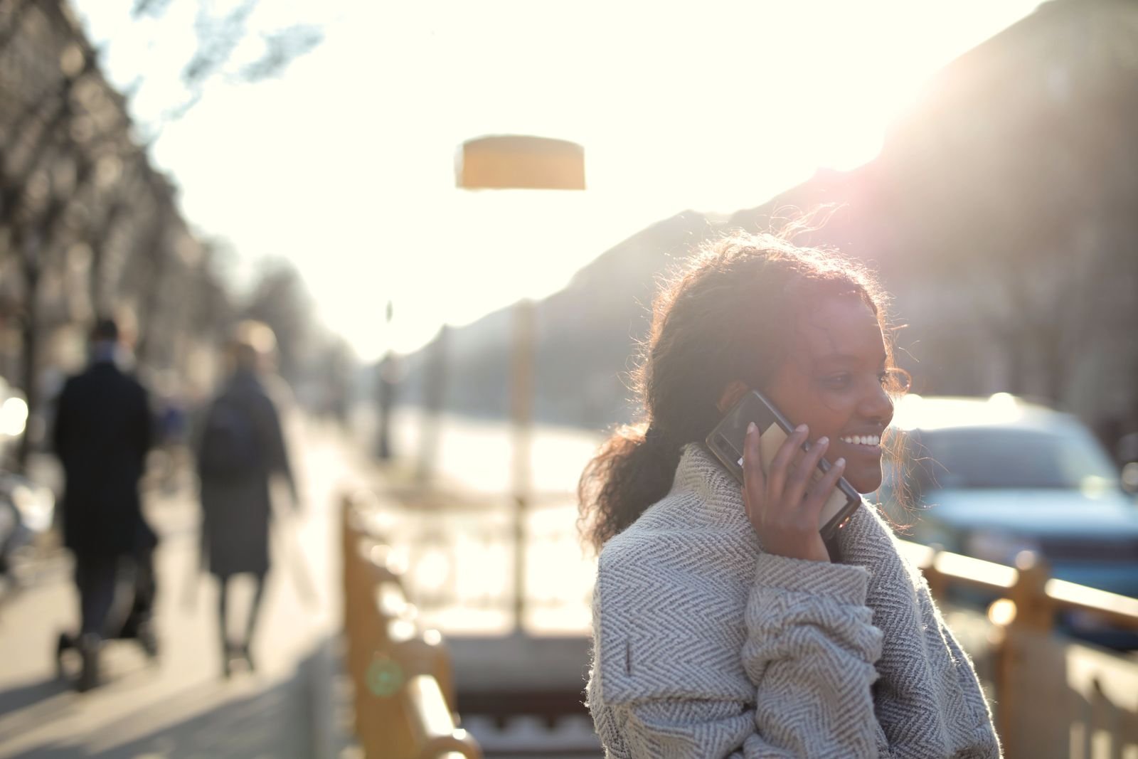 Smiling woman having a relaxed phone conversation outdoors, the back-and-forth style Gemini handles better than Assistant