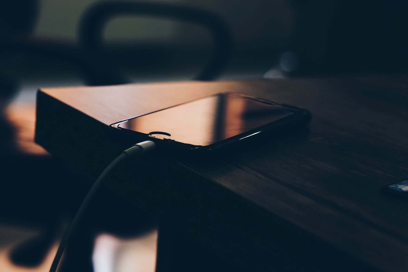 iOS 27 Is Draining iPhone Batteries. Here's What Apple Actually Says. 1 Phone plugged into a charger on a dark wooden desk