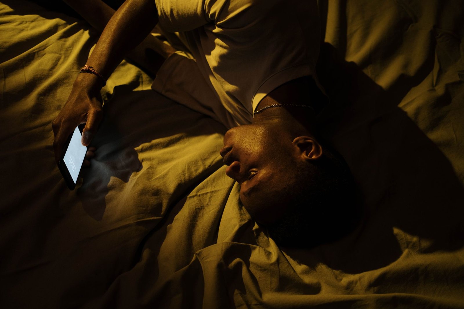 Man scrolling his phone in bed at night, the moment most AI investment scams find their target
