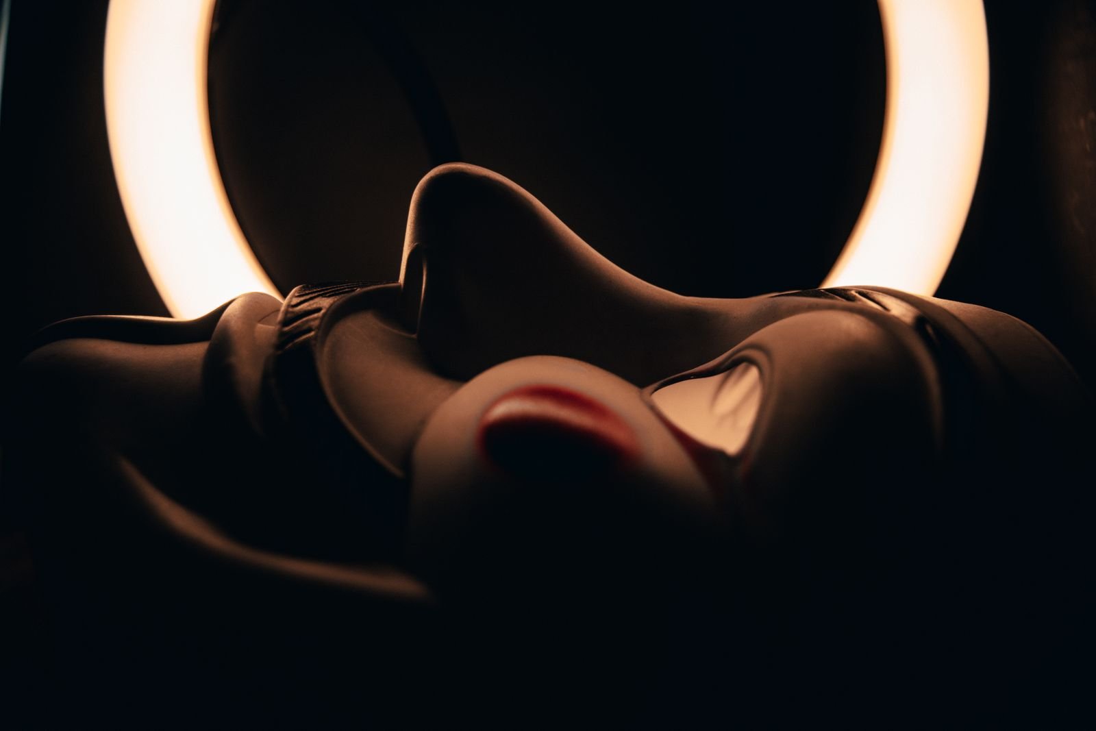 A mask lit by a ring light in a dark room, a stand-in for an AI persona built for the feed