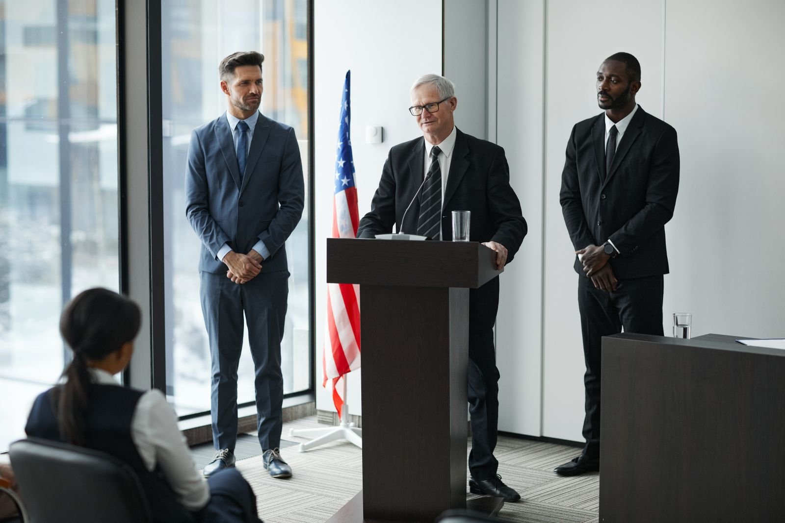 Officials speaking in front of an American flag, standing in for the White House response to the AI slowdown call