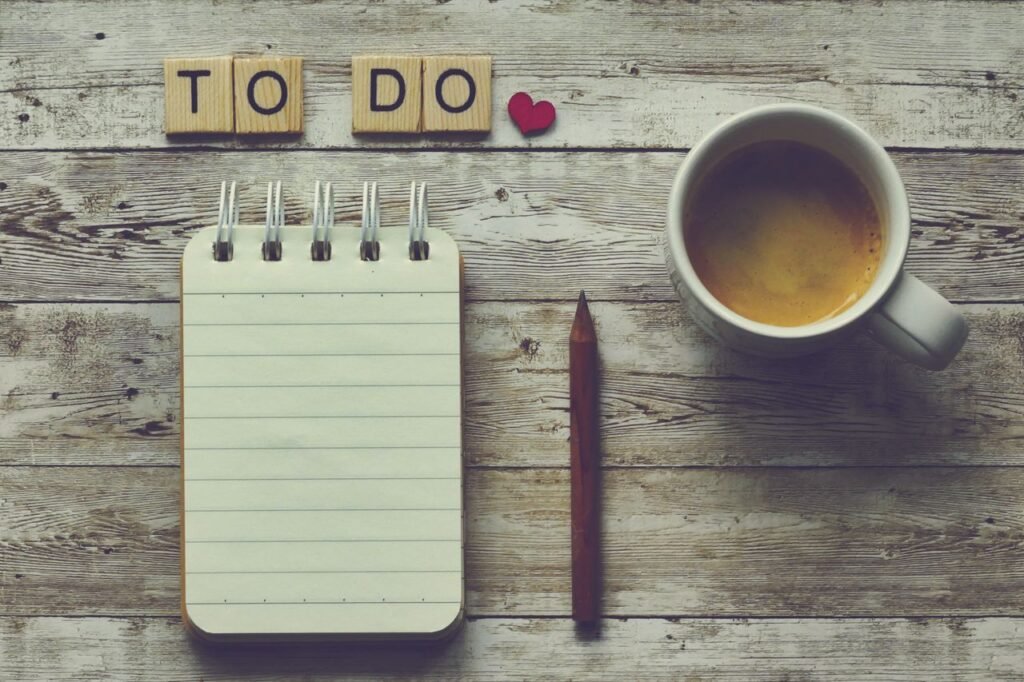 Flat lay of a notebook, pencil, coffee cup, and 'To Do' tiles on a rustic wooden table.