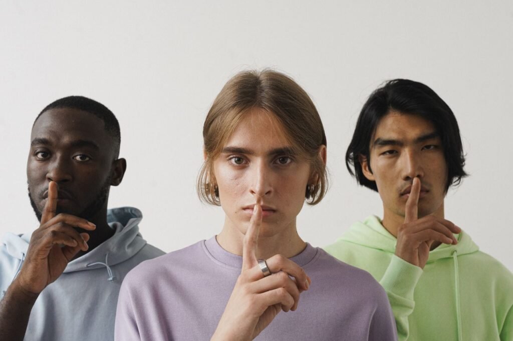 Three young adults making a shushing gesture in a studio setting, highlighting diversity.