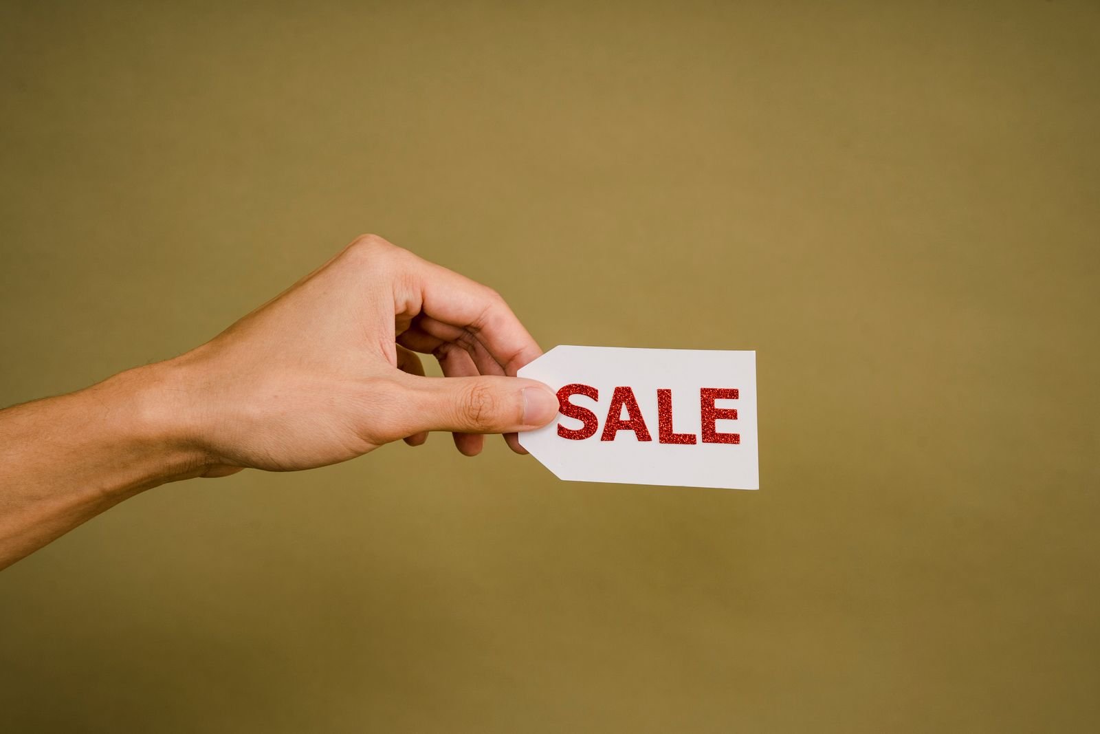 AI Memory Chip Prices Are Raising the Cost of Your Next Phone. Here's the Math. 3 A hand holding a small white sale tag, for the section on how to spend less while memory prices stay high