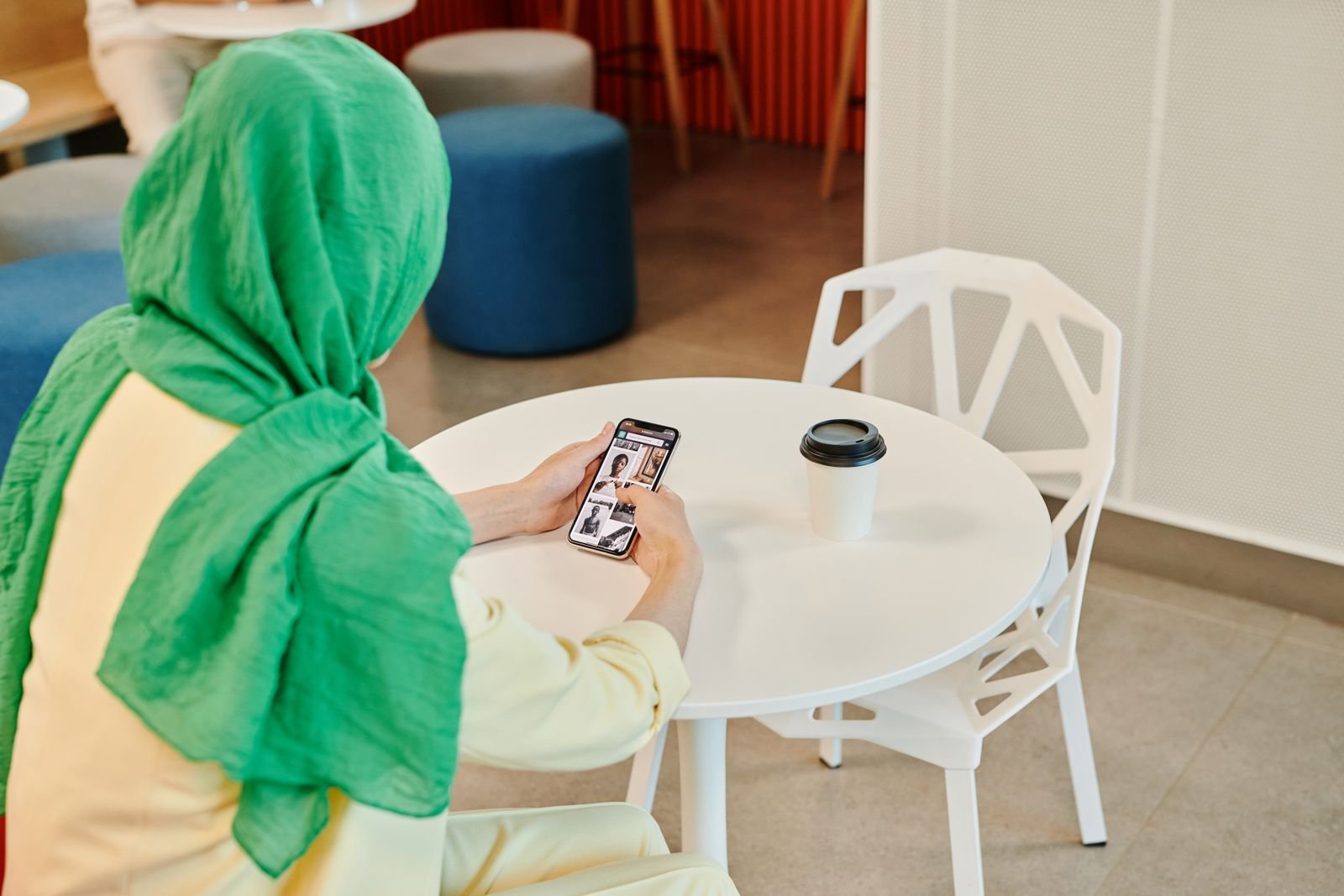 A woman scrolling her phone at a cafe table, the kind of feed where the Instagram AI-generated profile label will now show up