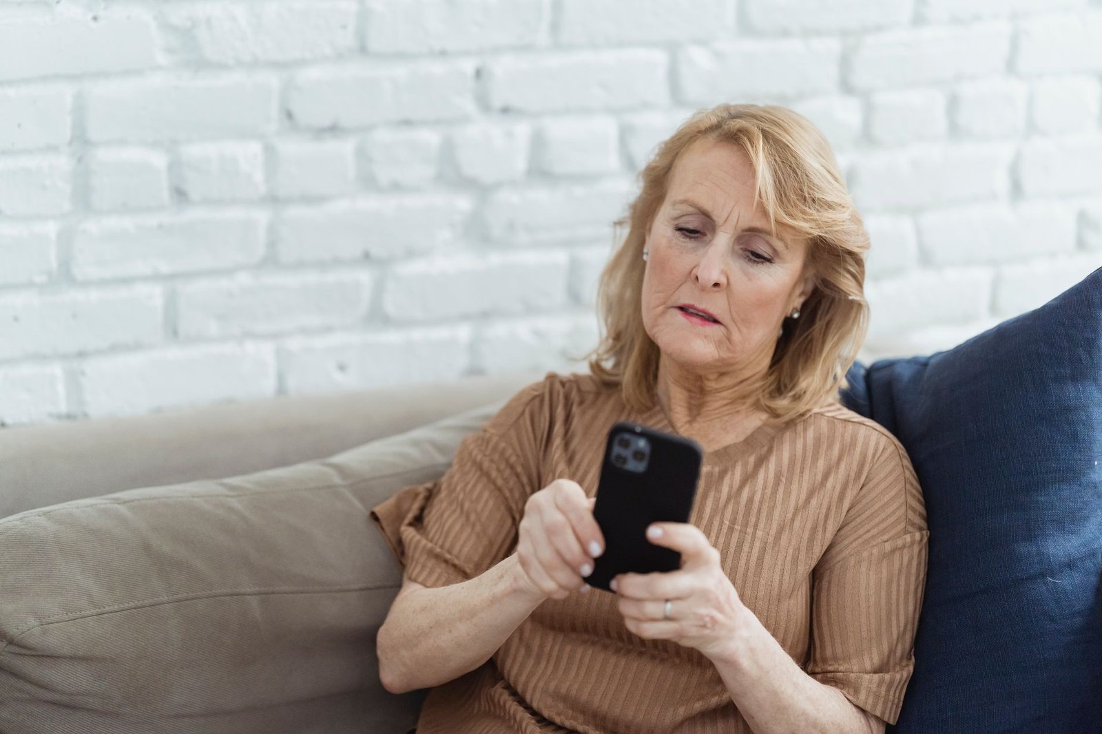 Older woman alone on a sofa using her phone, the entry point for most AI investment scams aimed at people over 60