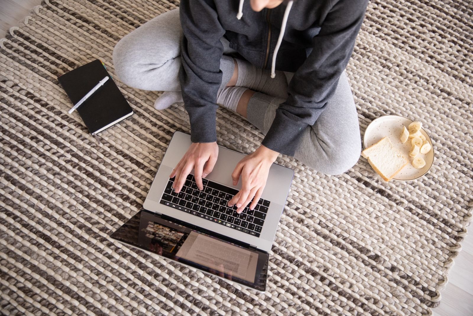A person sitting on a rug typing on a laptop with a notebook beside them, the way most people write emails with Claude